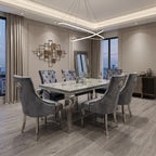 A modern dining room featuring a rectangular glass-top dining table with six tufted gray upholstered chairs, set in a contemporary room with wood floors and large windows.