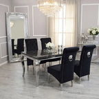 A luxury dining room set featuring a rectangular black marble-top table with silver legs and four matching high-back black velvet chairs with silver nailhead trim and lion ring backrests, set in a modern gray dining room with a large floor mirror.