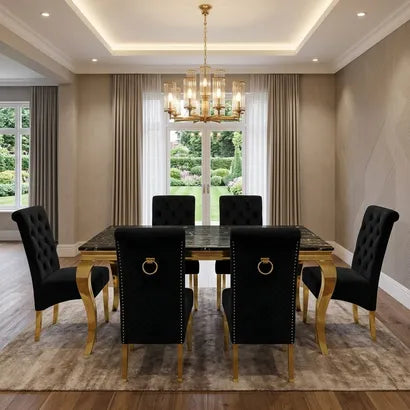 A luxury dining room set featuring a rectangular dark marble-top table with gold legs, surrounded by six black tufted velvet chairs with gold ring pulls and nailhead trim, set on a textured area rug under a gold chandelier.