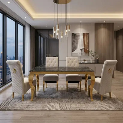 A modern dining room set featuring a rectangular dark marble-top table with ornate gold legs, surrounded by four tufted cream upholstered dining chairs and two matching stools, set on a patterned area rug in a contemporary loft.