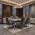 A modern dining room set featuring a rectangular marble-top dining table surrounded by six gray tufted velvet chairs, set on a patterned area rug in a luxury high-rise apartment with a city view at dusk.