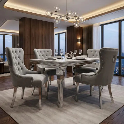 A luxury dining room set featuring a rectangular marble-top dining table with a polished chrome mirrored base, surrounded by four high-back tufted gray velvet chairs with silver nailhead trim, set on a light beige rug in a modern high-rise apartment.