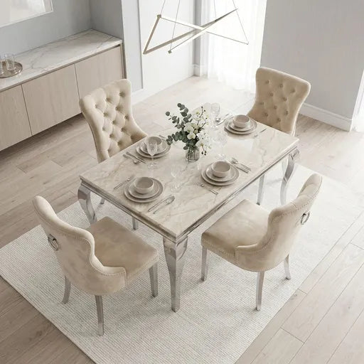 A modern dining room set featuring a rectangular marble-top table surrounded by four tufted cream velvet chairs, styled with tableware and a floral centerpiece on a light rug.