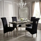 A luxury dining room set featuring a rectangular mirrored glass table with polished silver legs, surrounded by four black tufted velvet dining chairs with silver nailhead trim and silver legs. The room is styled with a large ornate silver mirror, a crystal chandelier, and light gray paneled walls.