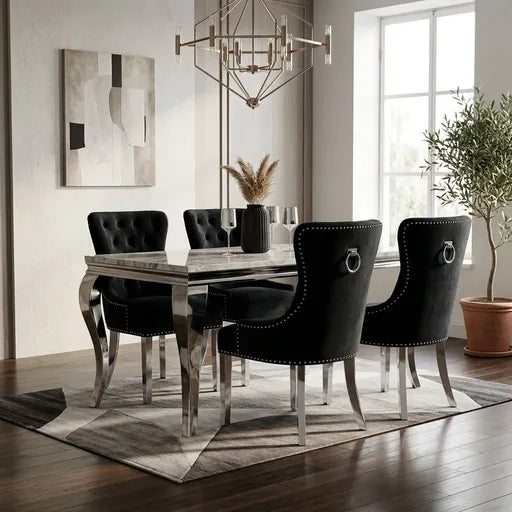 A modern dining room set featuring a rectangular table with a gray marble top and chrome legs, surrounded by four black velvet tufted chairs with silver nailhead trim and ring pulls, set on a geometric patterned rug.