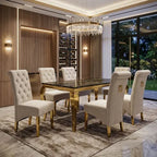 A luxury dining room set featuring a rectangular table with a polished black marble top and gold frame, surrounded by six tufted cream upholstered chairs with gold legs, set on a patterned rug under a crystal chandelier.