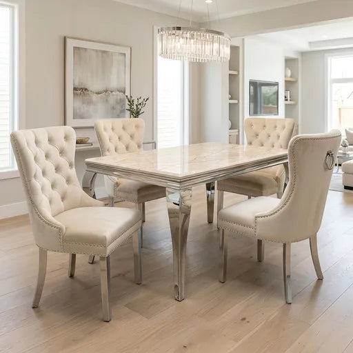 A luxury dining room set featuring a rectangular table with a polished silver marble top and mirrored legs, surrounded by four tufted cream upholstered dining chairs with silver nailhead trim.