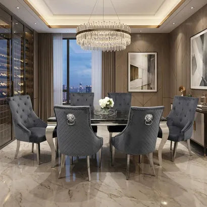 A modern dining room set featuring a rectangular white marble-top table with gold legs, surrounded by six tufted white upholstered chairs with gold accents, set on a textured gray rug in a contemporary dining room.