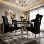 A luxury dining room set featuring a round chrome table and four black upholstered dining chairs with tufted and quilted backrests, styled in an elegant interior with a chandelier, geometric wall art, and a patterned rug.