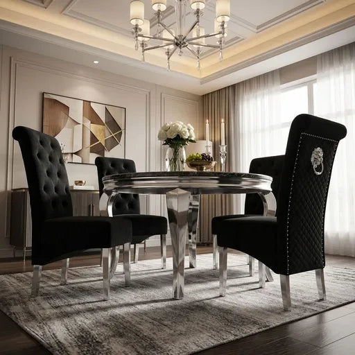 A luxury dining room set featuring a round chrome table and four black upholstered dining chairs with tufted and quilted backrests, styled in an elegant interior with a chandelier, geometric wall art, and a patterned rug.