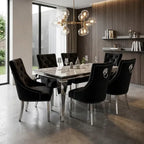 A modern dining room setup featuring a rectangular marble-top dining table surrounded by six black tufted velvet chairs with silver nailhead trim and chrome legs. A multi-light globe chandelier hangs above, set against a background of wood paneling and shelves.