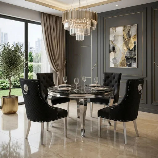 A luxury dining room setup featuring a round black marble-top dining table surrounded by four black tufted velvet chairs with silver nailhead trim and lion crest backrests. The room has dark gray paneled walls, a large crystal chandelier, and a potted tree in a gold pot.