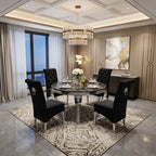 A luxury dining room setup featuring a round dark marble-top dining table surrounded by four black tufted high-back chairs with silver legs, set on a patterned area rug in a modern, elegant room with a crystal chandelier and wood-paneled walls.