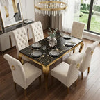 An elegant dining set featuring a rectangular black marble-patterned table with gold legs and six tufted cream upholstered chairs, styled in a modern dining room with a chandelier and large windows.