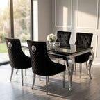 A luxury dining set featuring a rectangular black marble table with a polished silver frame, surrounded by four matching black tufted velvet chairs with silver lion head ring pulls and studded trim.