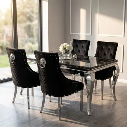 A luxury dining set featuring a rectangular black marble table with a polished silver frame, surrounded by four matching black tufted velvet chairs with silver lion head ring pulls and studded trim.