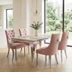 A modern dining set featuring a rectangular table with a light marble top and mirrored legs, surrounded by four pink tufted and quilted velvet chairs in a bright, contemporary dining room.