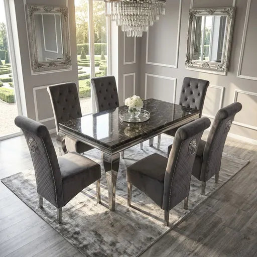 A luxury dining set featuring a rectangular table with a polished black marble top and mirrored silver legs, surrounded by six tufted and quilted gray velvet chairs with silver nailhead trim, set on a gray patterned rug in a bright, elegant dining room.