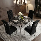 A luxury dining set featuring a round black marble table with a polished silver pedestal base, surrounded by four black upholstered dining chairs with tufted and quilted backrests, shown in a styled dining room setting.