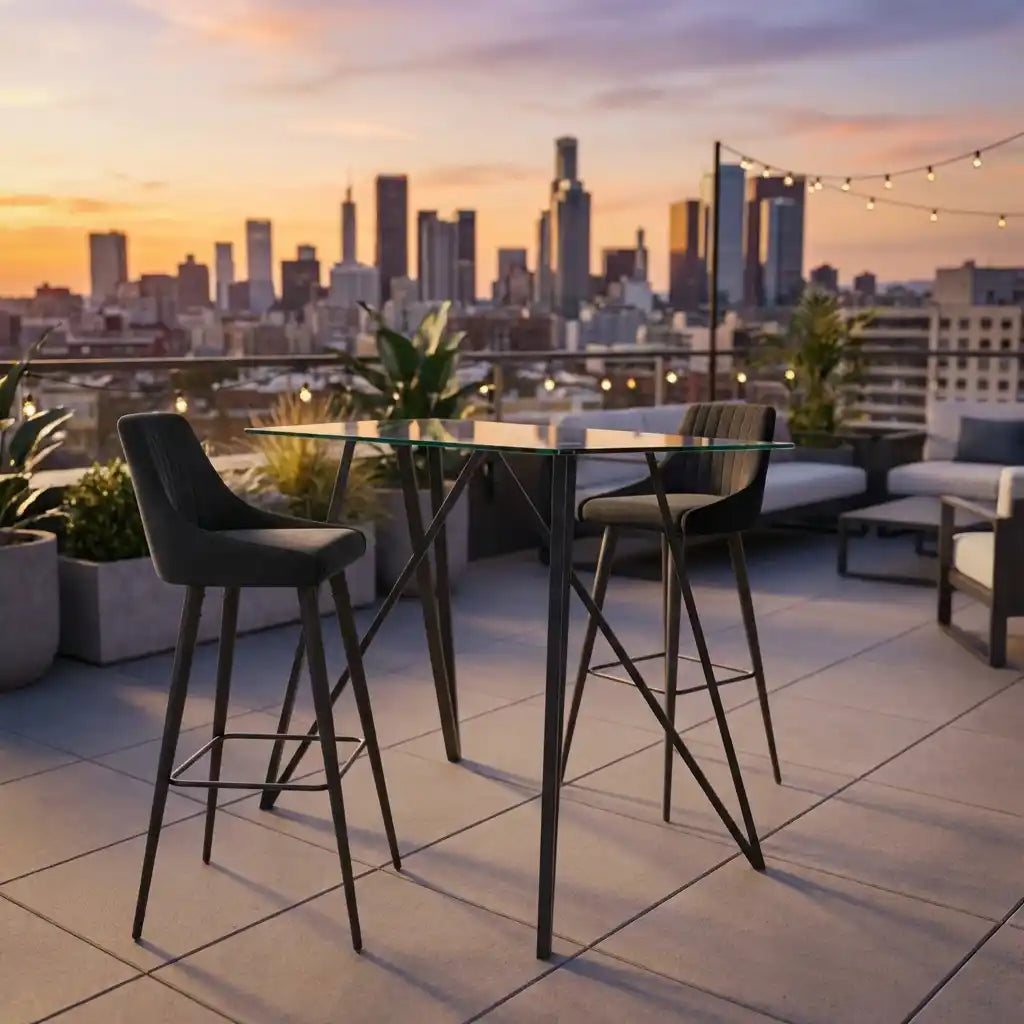 Outdoor seating area with high tables and chairs on a rooftop with city skyline in the background during sunset.