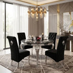 A luxury dining room set featuring a round marble-top table with a silver pedestal base and four black tufted velvet chairs with silver nailhead trim and lion head ring pulls, set on a geometric patterned rug in a modern, upscale interior.