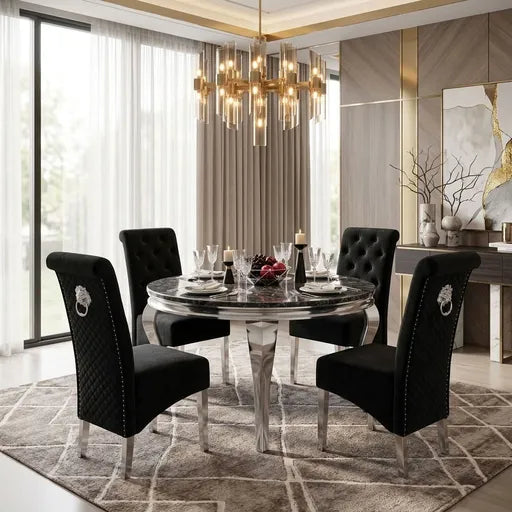 A luxury dining room set featuring a round marble-top table with a silver pedestal base and four black tufted velvet chairs with silver nailhead trim and lion head ring pulls, set on a geometric patterned rug in a modern, upscale interior.
