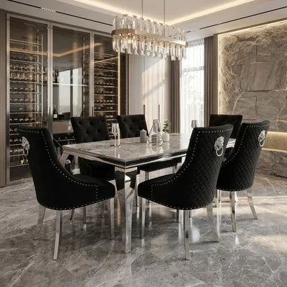 A luxury dining room set featuring a rectangular marble-top dining table surrounded by six black tufted velvet chairs with silver metal legs and decorative lion head accents on the backrests. The room is styled with a modern crystal chandelier, marble flooring, and a wine cellar in the background.