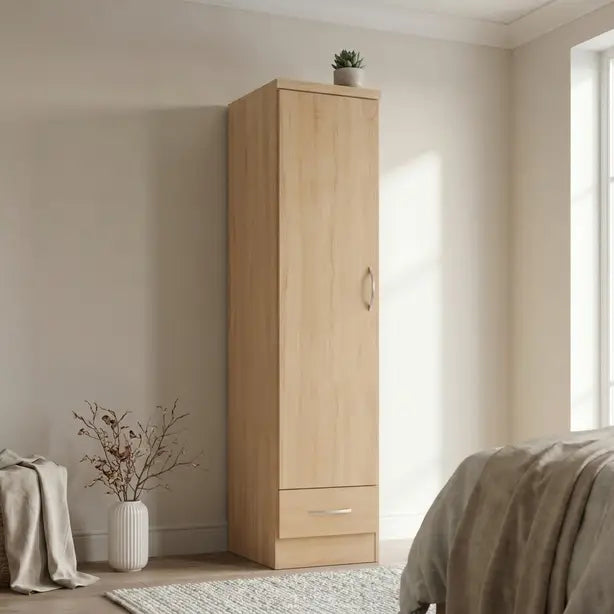 A tall, light oak wood wardrobe with a single door and a bottom drawer, styled in a minimalist bedroom setting.