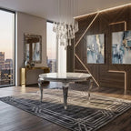 A modern dining room featuring a round marble-top table with ornate silver legs, set on a geometric patterned rug. The room has a dark wood accent wall with built-in LED lighting, two abstract art prints, a gold console table with a mirror, and a large crystal chandelier hanging from the ceiling.
