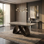 A modern dining table with a rectangular stone-look top and sculptural curved metal base, shown in a contemporary dining room setting with a rug, wall art, and pendant lights.