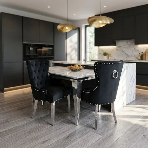 A modern dining two black tufted velvet chairs with silver nailhead trim and ring pulls, set in a contemporary kitchen with dark cabinets, marble island, and gold pendant lights.