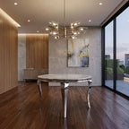 A modern round dining table with a polished marble top and curved metallic legs, set in a contemporary dining room with dark wood floors, a glass wall, and a hanging chandelier.