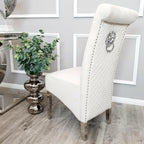 Cream upholstered chair with decorative backrest in a room with framed pictures on the wall.
