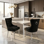 Two black tufted velvet dining chairs with silver nailhead trim and ring pulls, positioned at a white dining table in a modern kitchen setting.