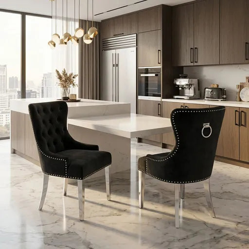 Two black tufted velvet dining chairs with silver nailhead trim and ring pulls, positioned at a white dining table in a modern kitchen setting.