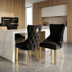 Two black velvet dining chairs with gold legs and nailhead trim, shown in a modern kitchen setting. One chair features a tufted back with a gold lion emblem.