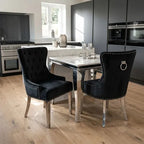 Two black velvet dining chairs with silver nailhead trim and ring pulls, positioned around a marble-top dining table in a modern kitchen setting with light wood floors.