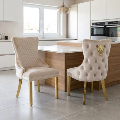 Two elegant tufted dining chairs in cream upholstery with gold legs, displayed in a modern kitchen setting.