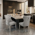 Two  gray tufted dining chairs with silver nailhead trim and metal legs, positioned at a kitchen island in a modern kitchen setting.