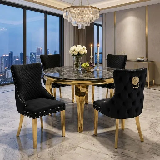 A luxury round dining table set with a polished gold base and a dark marble tabletop, surrounded by four black tufted velvet chairs with gold legs and silver nailhead trim, set in a modern high-end dining room.