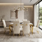 A modern dining room set featuring a rectangular white marble-top table with gold legs, surrounded by six tufted white upholstered chairs with gold accents, set on a textured gray rug in a contemporary dining room.