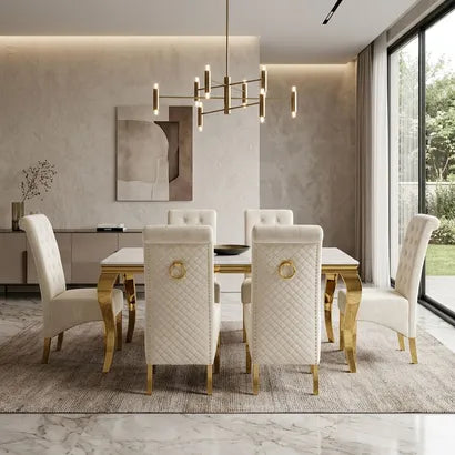 A modern dining room set featuring a rectangular white marble-top table with gold legs, surrounded by six tufted white upholstered chairs with gold accents, set on a textured gray rug in a contemporary dining room.