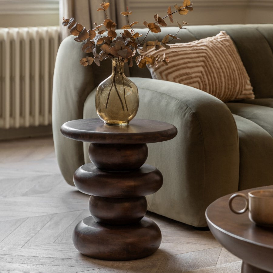 Wooden side table with a vase of dried leaves in a living room setting.