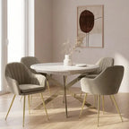A round white dining table with a gold-tone metal base and four upholstered dining chairs in a light taupe velvet fabric with gold legs, set in a bright, modern dining room.