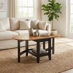 A round wooden coffee table with a dark metal frame and lower shelf, styled in a bright living room next to a beige sofa and a potted fiddle-leaf fig plant.
