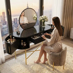 Woman sitting at a stylish vanity table with mirror and makeup items, in a room with large windows overlooking a cityscape.