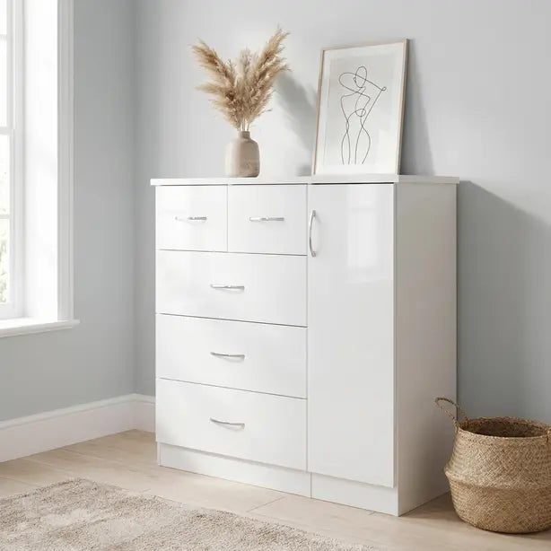 A tall white wooden chest of drawers with five drawers and a cabinet door, styled in a bright room with a vase of pampas grass and a framed print on top.