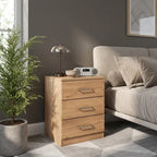 A three-drawer wooden nightstand with a light oak finish stands beside a bed in a modern bedroom. 