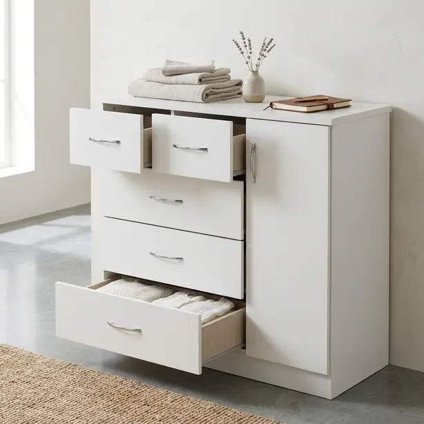 A white wooden storage cabinet with five drawers and one side door, shown in a bright room with one drawer open to reveal folded towels. Decorative items including folded towels, a small vase, and a book are placed on top.