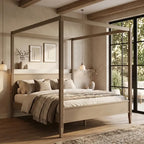 A light natural wood four-poster canopy bed with a matching headboard and footboard, styled in a warm, neutral-toned bedroom with beige walls, wooden ceiling beams, and a large window.